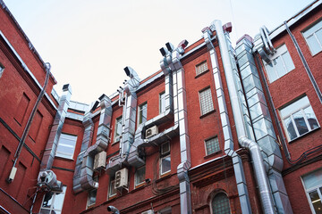 Obraz premium the building's exterior is made of red brick, with lots of shiny stainless steel pipes running through it. air outlets for air conditioner