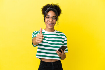 Young african american woman isolated on yellow background using mobile phone while doing thumbs up