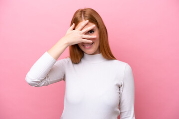 Young redhead woman isolated on pink background covering eyes by hands and smiling
