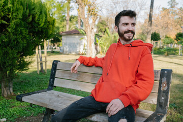 Obraz premium Young smiling man sitting on old park bench and looking to future.