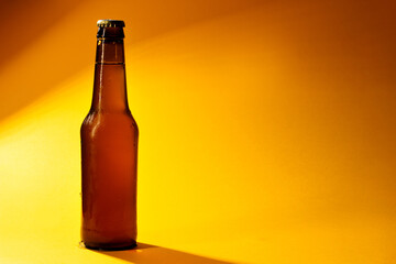bottle of cold beer closed on yellow background with shadows