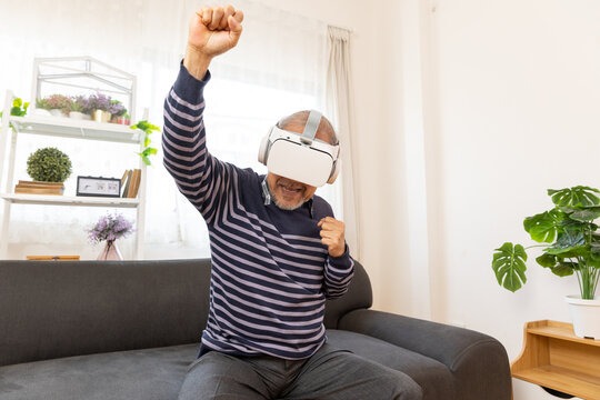 Senior man using VR headset to explore augmented reality at home in living room . Disabled elderly male playing virtual online game, having fun with modern technologies.