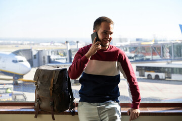 young man smiles confident while talking on his phone from the airport