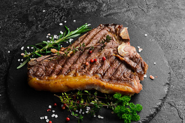 Grilled t-bone beef steak. Steak on a black plate. Top view. On a black stone background.