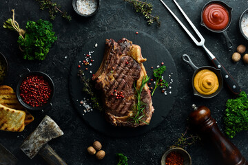 cowboy steak with spices on a stone background, first-class rib on the bone, top view. On a black stone background.