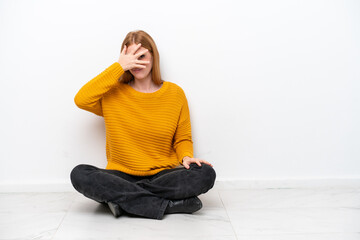 Young redhead woman sitting on the floor isolated on white background covering eyes by hands and...