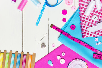 Pink and blue fabrics, various buttons, tools and accessories for sewing on a white wooden table
