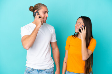 Young caucasian couple isolated on blue background talking to mobile