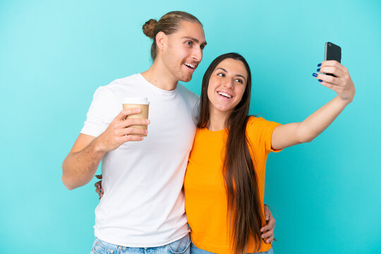 Young caucasian couple isolated on blue background making a selfie with the mobile