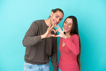 Young caucasian couple isolated on blue background making a heart with hands