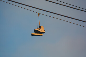 Close up of old sneakers hanging on a power line in the evening glow - Powered by Adobe