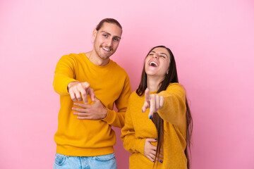 Obraz premium Young caucasian couple isolated on pink background pointing with finger at someone and laughing a lot