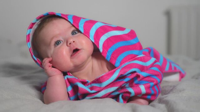 Cute happy baby toddler girl in striped bathrobe with hoodie is with her hand up to his chubby cheek.