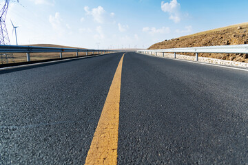 Empty asphalt highway road surrounded by fields with windmills