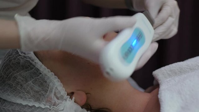 Ultrasonic face cleaning in a beauty salon. Woman receives a youth and skin care procedure. Cosmetologist cleans female face with hardware technique