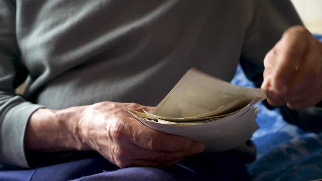 An aged man examines a family photo archive. The hands of a pensioner holding old family black and white photographs. Nostalgia, memories of an elderly person. selective focus