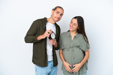Young caucasian couple isolated on white background pregnant and holding clock