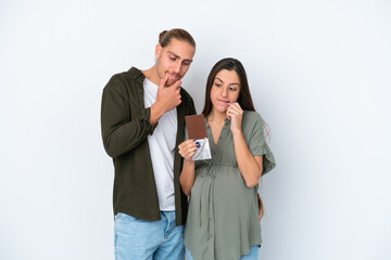 Young caucasian couple isolated on white background pregnant and having doubts while holding chocolate