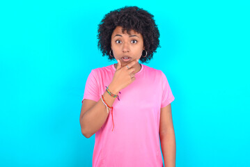young girl with afro hairstyle wearing pink T-shirt over blue background Looking fascinated with...