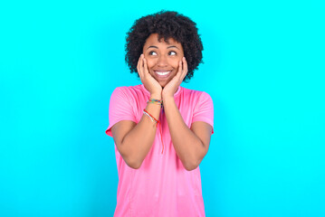 Inspired young girl with afro hairstyle wearing pink T-shirt over blue background looking at copyspace having thoughts about future events
