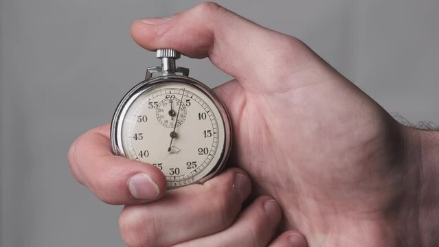 Stopwatch in hand. Analogue Stop-watch in Man Hand counts down seconds. Close-up. Male hand holding retro old vintage clock timer. Pushing the mechanical stopwatch button.
