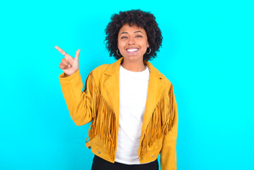 Young woman with afro hairstyle wearing yellow fringe jacket over blue background pointing up with...