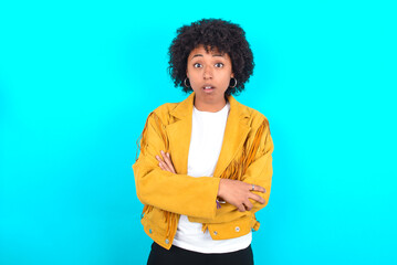 Shocked embarrassed Young woman with afro hairstyle wearing yellow fringe jacket over blue...