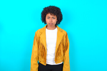 Offended dissatisfied Young woman with afro hairstyle wearing yellow fringe jacket over blue...