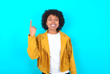 Young woman with afro hairstyle wearing yellow fringe jacket over blue background smiling and...