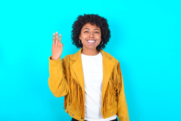Fototapeta na wymiar Young woman with afro hairstyle wearing yellow fringe jacket over blue background smiling and looking friendly, showing number three or third with hand forward, counting down