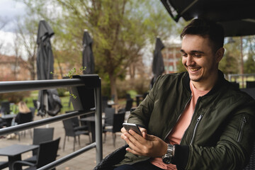 A one man is sitting alone outdoors drinking coffee and using his phone during the day