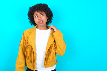 Young woman with afro hairstyle wearing yellow fringe jacket over blue background stressed, anxious, tired and frustrated, pulling shirt neck, looking frustrated with problem