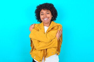 Charming pleased Young woman with afro hairstyle wearing yellow fringe jacket over blue background...