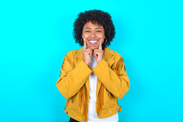 Happy Young woman with afro hairstyle wearing yellow fringe jacket over blue background with toothy...