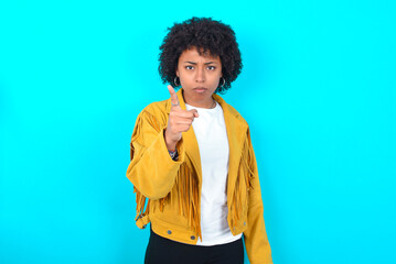 Young woman with afro hairstyle wearing yellow fringe jacket over blue background frustrated and...