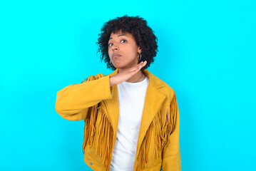 Young woman with afro hairstyle wearing yellow fringe jacket over blue background cutting throat...