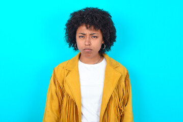 Young woman with afro hairstyle wearing yellow fringe jacket over blue background Pointing down with fingers showing advertisement, surprised face and open mouth