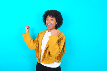 Hooray cool Young woman with afro hairstyle wearing yellow fringe jacket over blue background point...