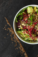 Vegetarian salad with cucumbers, lettuce, walnuts and flax seeds in a round takeaway paper container on dark background.Healthy food, restaurant dish delivery. Top view. Free space for text
