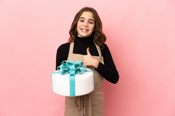 Little Pastry chef holding a big cake isolated on pink background giving a thumbs up gesture