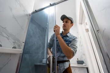 Workers are installing glass door of the shower enclosure.