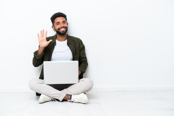 Young Brazilian man with a laptop sitting on the floor isolated on white counting five with fingers