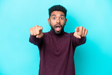 Young Brazilian man isolated on blue background surprised and pointing front