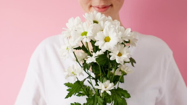 A young woman sniffs and enjoys a bouquet of daisies. Pink background. The concept of March 8 and spring.