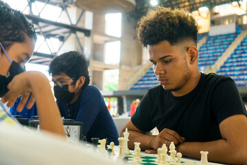 Young Latin man thinking about his move during a chess game in a gym. Concept of intelligence and...