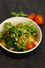 Vegetarian salad with potato, tomatoes, arugula and 
pumpkin seeds in round paper take-away container on dark background. Healthy food delivery concept. Free space for text.
