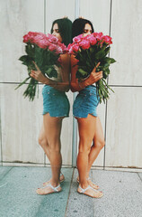 Fit young brunette woman in shorts holding bouquet of pink roses in the Summer city.