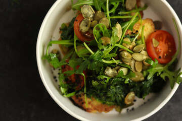 Vegetarian salad with potato, tomatoes, arugula and 
pumpkin seeds in round paper take-away container on dark background. Healthy food delivery concept. Close-up.