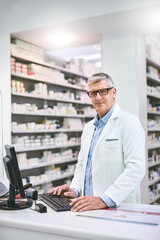 So many meds to choose from. Portrait of a confident mature male pharmacist typing on a computer...