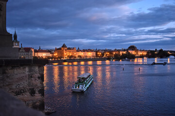 Naklejka premium View from charles bridge in Prague on old houses with reflections and a small ship in the water.